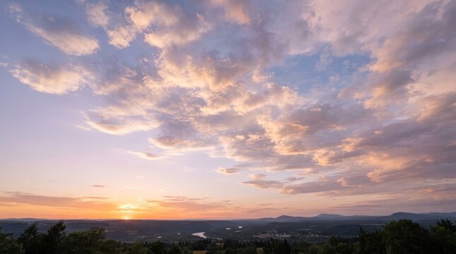 Serene sunset illuminates sky with cumulus clouds over rolling hills and distant mountains