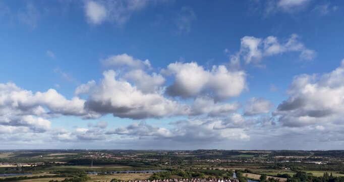 Aerial footage rising above Castleford in Yorkshire revealing expansive countryside waterways green fields distant residential areas and farmland beneath a wide blue sky filled with clouds