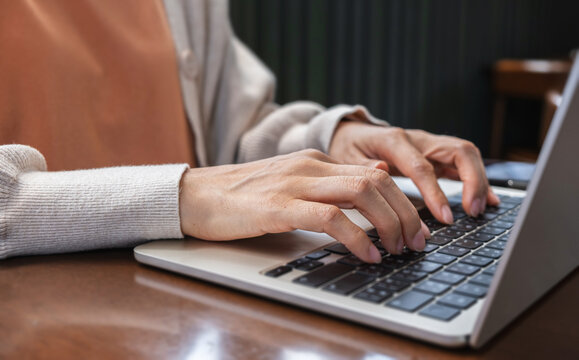 Close up female hands typing on laptop computer keyboard while working on wooden table in cafe.