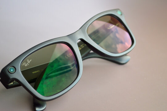 Smart glasses with colorful iridescent reflective lenses and built-in camera resting on a clean gray surface in modern tech product photography
