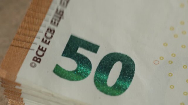 A macro shot showing a stack of 50 euro banknotes being counted or flicked through, highlighting the holographic ink and paper texture. Useful for finance and economy concepts.