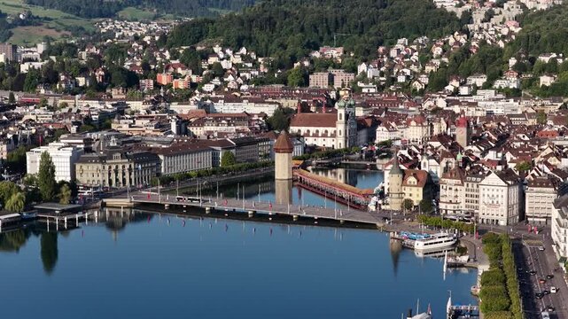 Panoramic view across Lucerne toward the historic waterfront, with the Chapel Bridge, lakefront promenade, harbor and densely built city center surrounded by wooded hills.