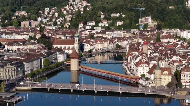 Detailed aerial perspective of Lucerne's historic center, highlighting the Chapel Bridge and Wasserturm over the Reuss River with traditional buildings and Lake Lucerne nearby.