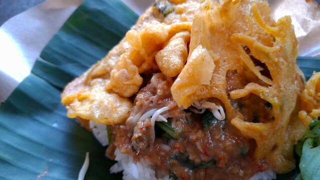 Nasi pecel with peanut sauce and vegetables, and fried tempeh, served on a banana leaf