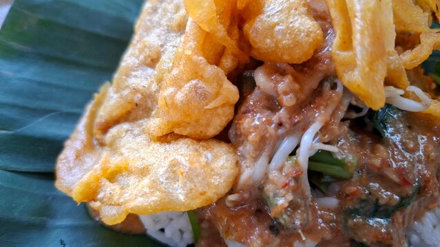 Nasi pecel with peanut sauce and vegetables, and fried tempeh, served on a banana leaf