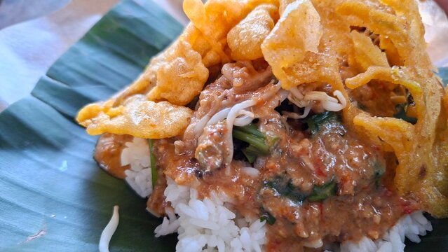 Nasi pecel with peanut sauce and vegetables, and fried tempeh, served on a banana leaf
