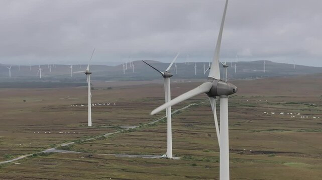An aerial drone shot of a large wind farm located on a peat bog in West Ireland, showcasing ecofriendly renewable energy production under a cloudy sky.
