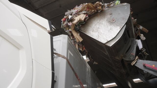 Wheel loader dumping mixed paper and cardboard into a large container inside an industrial recycling facility.