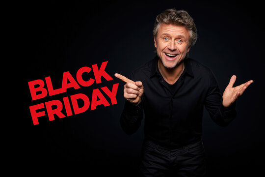 Man excited about Black Friday deals, pointing at the text with a smile, isolated on a black background, symbolizing shopping and discounts.