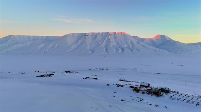 Push forward glides toward the dog sled camp and its kennel rows, the distant peaks catching a brief warm alpenglow above the quiet Svalbard valley