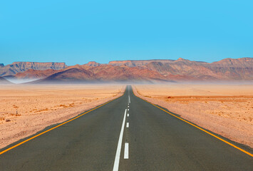 Obraz premium Beautiful empty asphalt dirt road in desert plain with mountains in background - Namibia, Africa