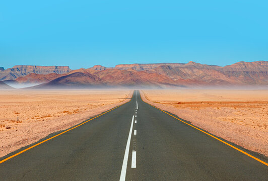 Beautiful empty asphalt dirt road in desert plain with mountains in background - Namibia, Africa
