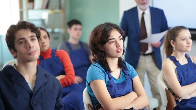 Focused young worker trainees looking ahead during educational seminar with senior educator standing behind 