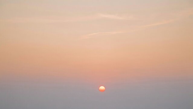 Vibrant round sun disc glowing brightly in a soft pastel colored sky during a peaceful and calm golden hour sunset
