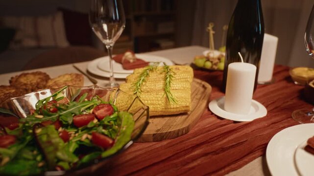 Festive Thanksgiving dinner table displaying cooked corn cobs, fresh salad, tartlets and wine glasses during zoom out. Footage suitable for culinary advertising and holiday food catering promos