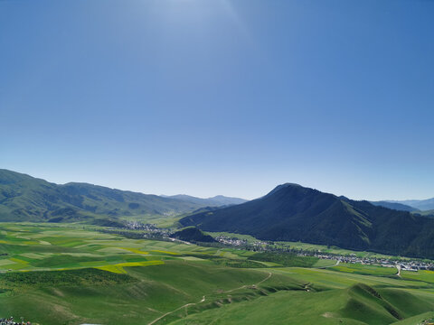 Rural valley with farmland, village and mountains under clear blue sky