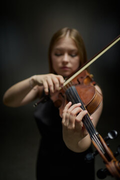 Vertical image of Caucasian young adult girl playing violin during musical performance. Classical musician practicing instrument for music school advertising, concert promotion