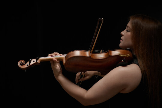 Caucasian young adult woman playing classical violin during music concert performance. Ideal visual asset for orchestra advertising, music education campaigns, and instrument promotion