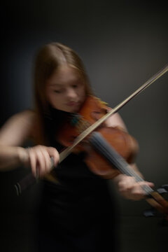 Vertical shot of young Caucasian female violinist playing violin with motion blur effect. Dynamic musical performance visual suitable for classical concert advertising and arts education