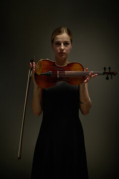 Vertical portrait of young adult Caucasian woman holding violin with bow horizontally. Professional musician representing classical music education, concert advertising
