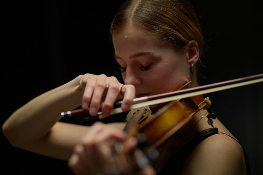Young adult Caucasian woman playing violin during concert rehearsal, close up shot. Scene suitable for classical music education, performing arts marketing, and cultural event promotion