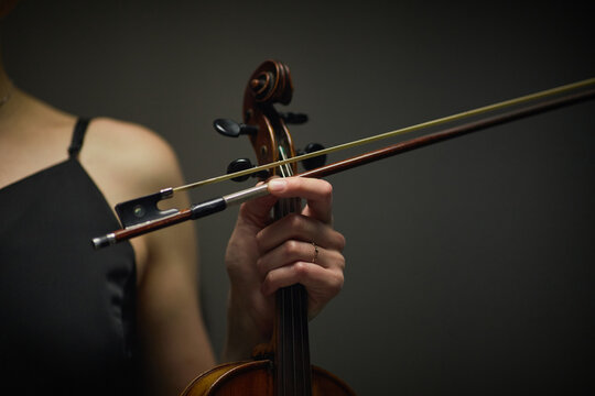 Young adult Caucasian female musician holding violin bow and fingerboard during classical concert performance. Ideal for music school promotion and orchestral event marketing