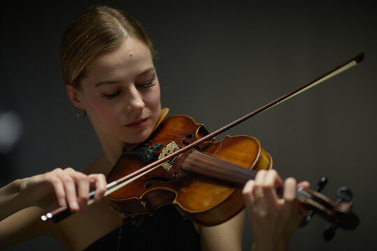 Young adult Caucasian woman playing acoustic violin with eyes closed during rehearsal. Visual suitable for classical music education, performing arts marketing, concert promotion campaigns