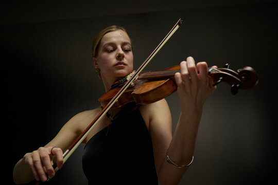 Young adult Caucasian female musician playing violin during classical concert performance. Image suitable for arts education, symphony orchestra promotions, music school marketing