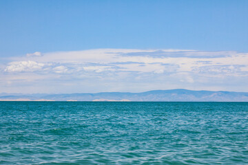 Fototapeta premium Calm blue lake with distant mountains under a bright cloudy sky