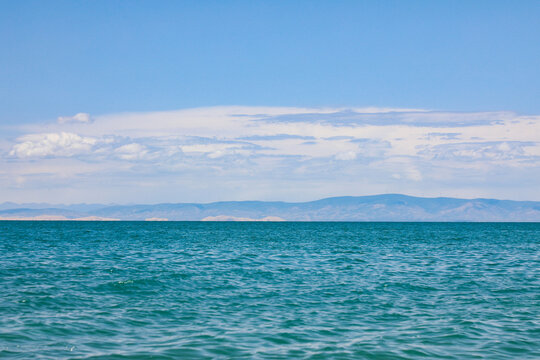Calm blue lake with distant mountains under a bright cloudy sky