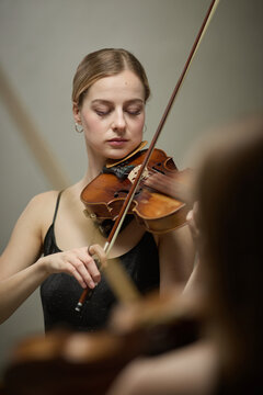 Vertical shot of young adult Caucasian woman playing violin with closed eyes during music rehearsal. Image suitable for classical concert advertising and arts education