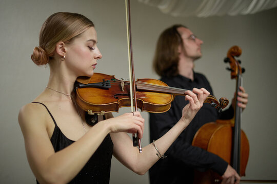 Caucasian young adult woman playing violin near Caucasian young adult man with cello in music rehearsal. Perfect for classical concert advertising and arts education campaigns