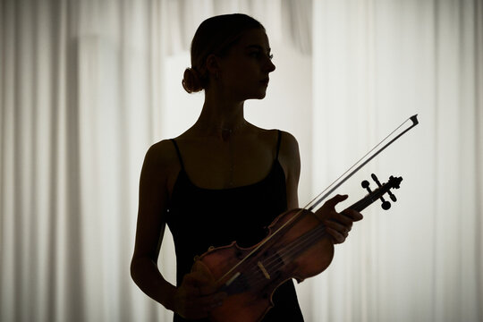 Young adult Caucasian woman holding violin with bow, practicing classical music performance. Image suitable for concert advertising and music academy marketing