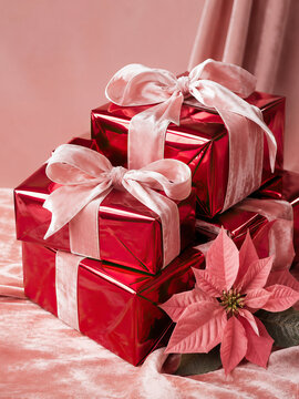 Gift boxes wrapped in shiny red paper with satin pink bows sit on a plush pink velvet surface. New Year and Christmas holiday concept.