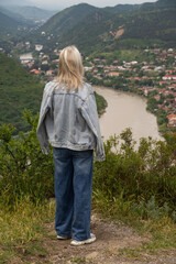Woman standing on a hill admiring the panoramic landscape view of Mtskheta town, framed by green mountains with the Kura river winding through the valley. Vertical photo © yaroslav1986