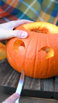Vertical video: Close-up of human hands carving a spooky scary face on a Halloween pumpkin with a knife. DIY holiday decoration process. 9:16 format.