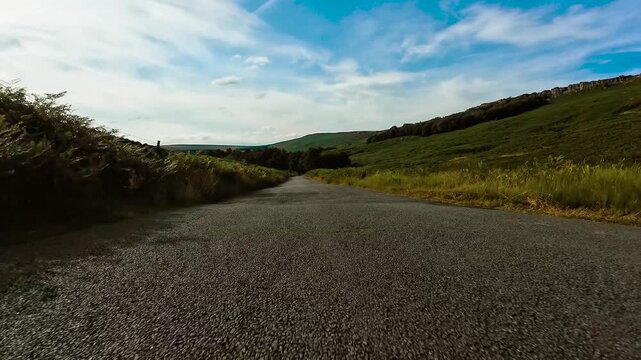 Car driving along winding rural road through rolling hills with dashboard camera perspective POV. Driver perspective on countryside highway with scenic green landscape and asphalt road point of view