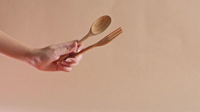 Hand holding eco-friendly wooden spoon and fork against beige background
