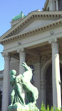 Serbian Parliament central entrance: Toma Rosandic sculptures and portico with columns, capitals, pediment, and dome. Illustrates  Beaux-Arts influence and ceremonial architecture in Belgrade.