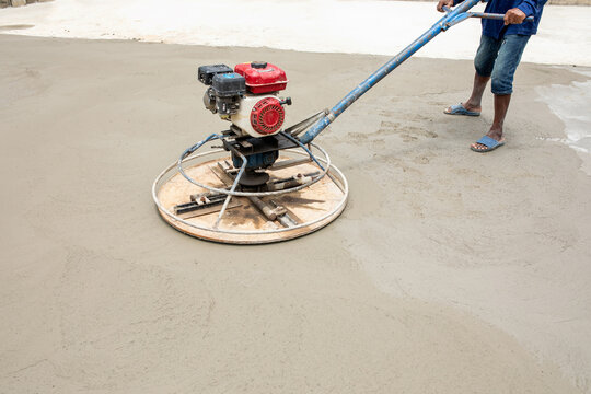 Power trowel machine glides smoothly across freshly poured concrete surface, spinning disk polishes gray floor to even finish, clean minimal composition highlights pure material detail