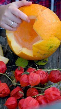 Vertical video: Close-up of human hands carving a spooky scary face on a Halloween pumpkin with a knife. DIY holiday decoration process. 9:16 format.