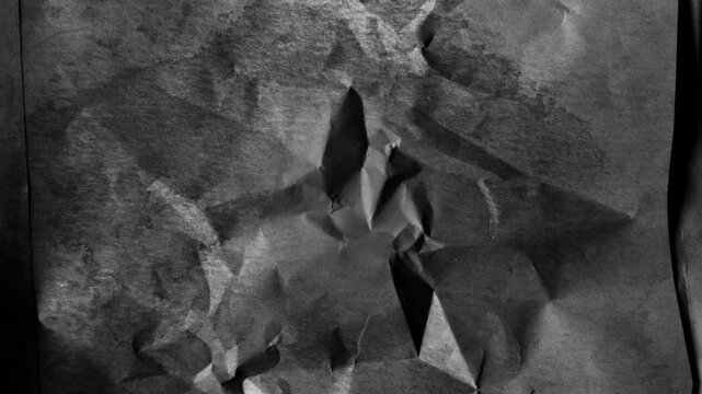 Abstract dark textured paper background with sharp geometric folds and deep shadows.