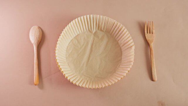 Stop motion of green leaves forming recycling symbol inside paper plate with wooden cutlery on brown
