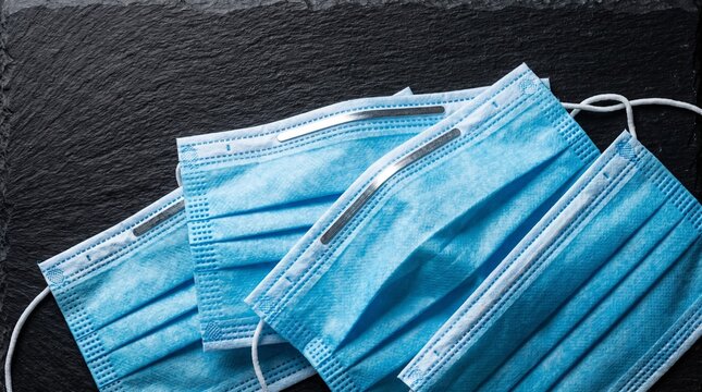 Stacked blue disposable surgical face masks showing nose clips on dark slate background, medical safety concept