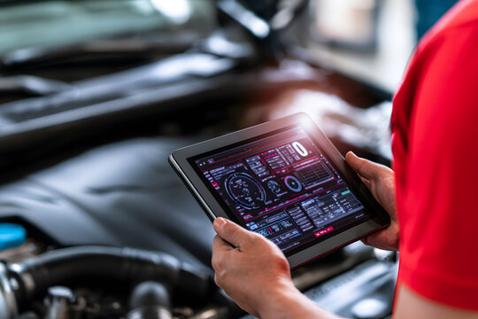 Close up of mechanic in red shirt holding tablet showing car engine diagnostic software. Professional automotive repair and high tech maintenance concept.