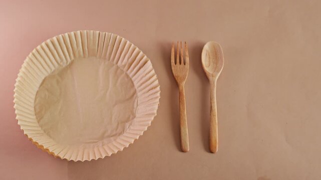 Stop motion animation of eco-friendly paper plate, wooden fork and spoon, and bowl appearing on brown