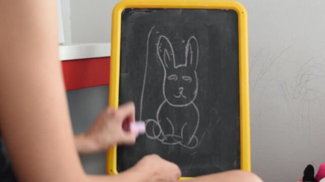 Woman illustrating a rabbit on a drawing board and explaining it to her children, close up