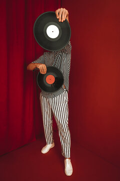 Person in striped suit holding vinyl records against red background