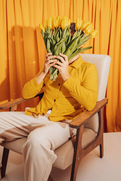 Man in yellow shirt holding tulip bouquet over face indoors