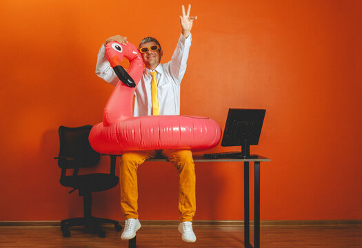 Smiling man wears flamingo float on office desk for summer vacation
